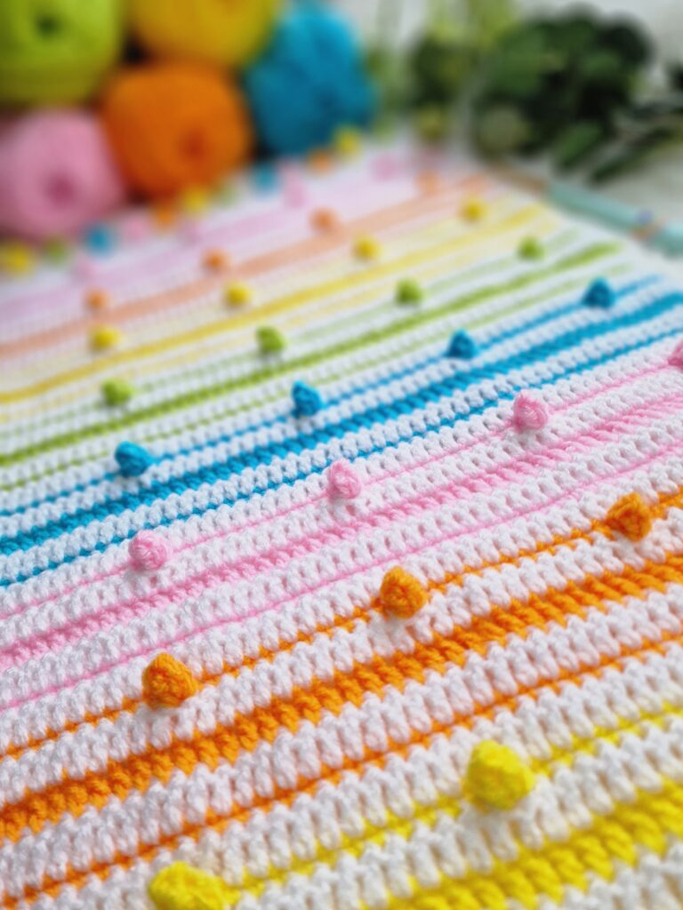 Close-up of the 'A Spot of Spring' crochet blanket by EmkatCrochet, featuring a detailed floral-inspired pattern in soft pastel yarns, draped gently to show texture and stitch work