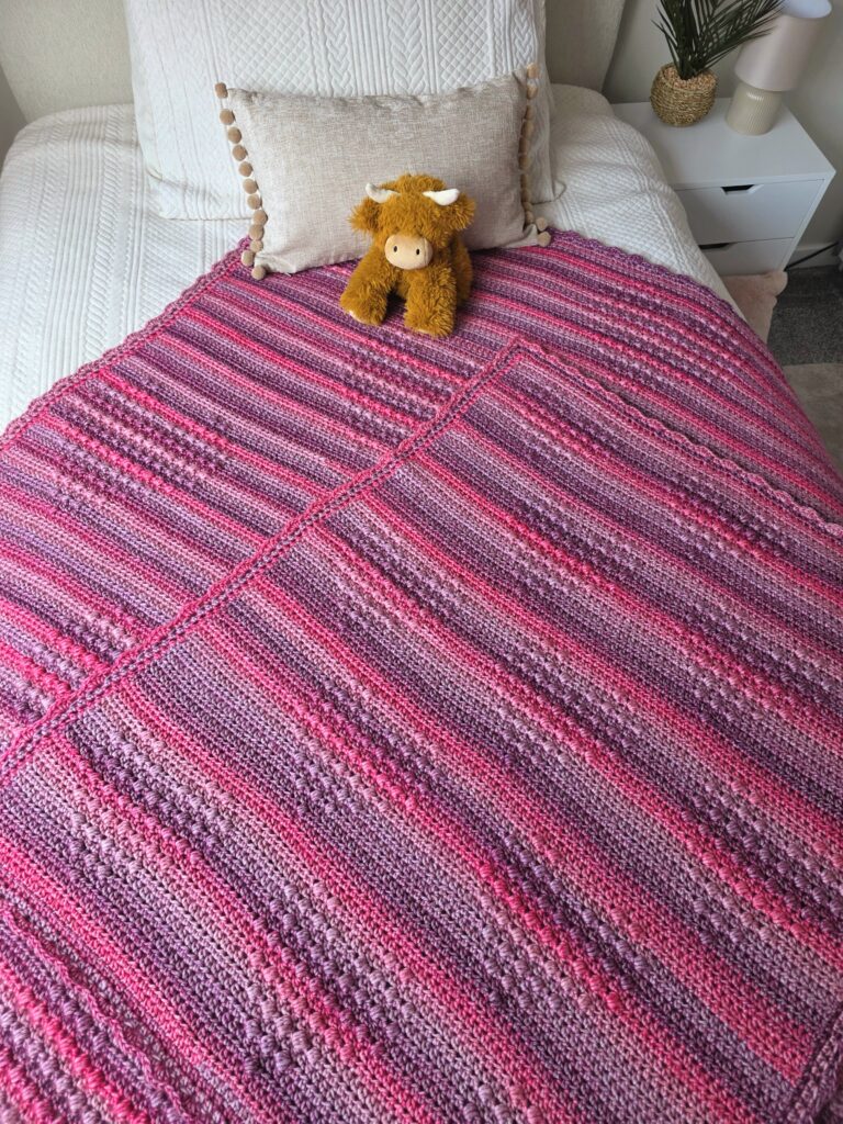 large and mini version of the hugs and hearts blanket by emkatcrochet - Hugs and Hearts blanket by EmkatCrochet, handmade in Yarnsmiths Pebble Haze Prints Aran yarn, showcasing textured heart motifs and cozy stitches in a soft, variegated color palette