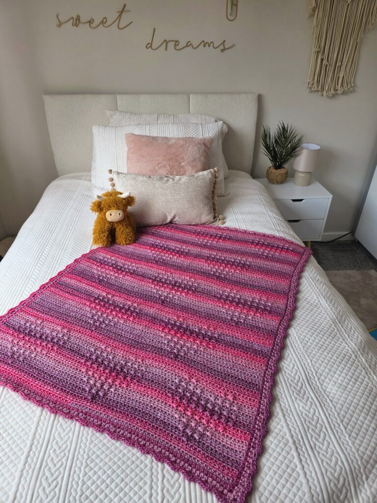 Hugs and Hearts blanket by EmkatCrochet, handmade in Yarnsmiths Pebble Haze Prints Aran yarn, showcasing textured heart motifs and cozy stitches in a soft, variegated color palette