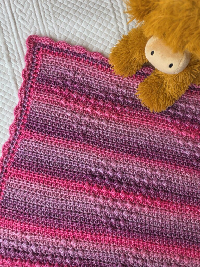 close up - Hugs and Hearts blanket by EmkatCrochet, handmade in Yarnsmiths Pebble Haze Prints Aran yarn, showcasing textured heart motifs and cozy stitches in a soft, variegated color palette
