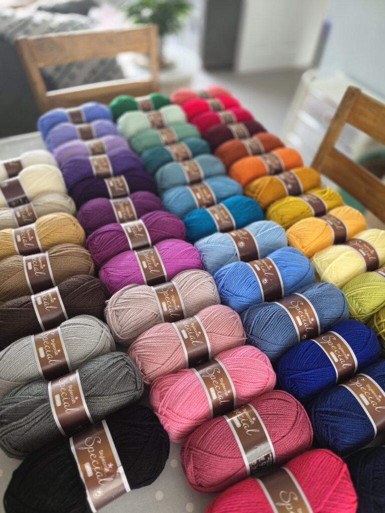 Full range of Stylecraft Special Aran yarn neatly displayed in rainbow order on a wooden table, showing a spectrum of vibrant and pastel shades