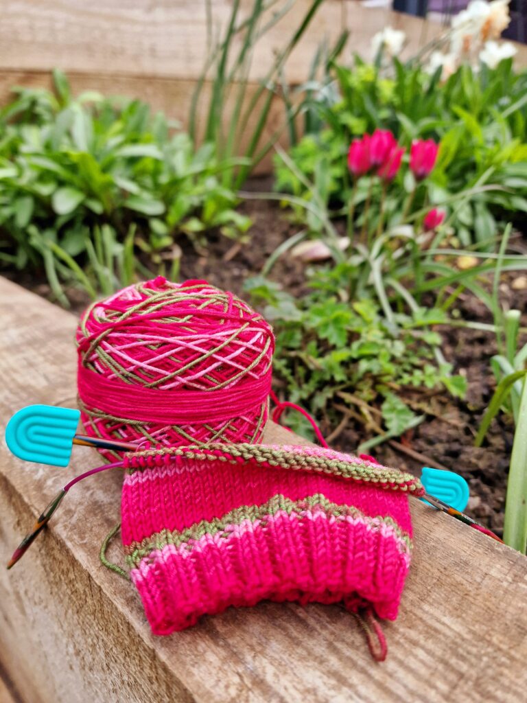 Hand-knitted socks in King Cole Footsie yarn, Watermelon colour, on KnitPro circular needles with a Muud Living tan leather project bag