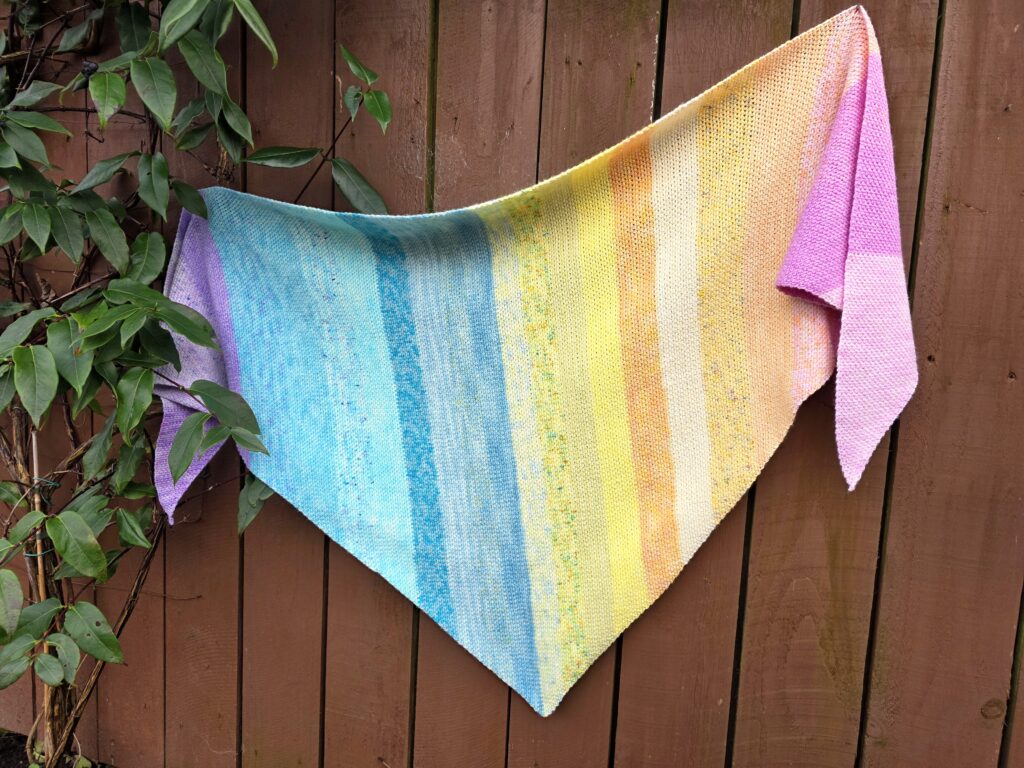 Crochet Magic Moss Stitch Shawl made with mini skeins, shown in soft rainbow stripes and draped outdoors.